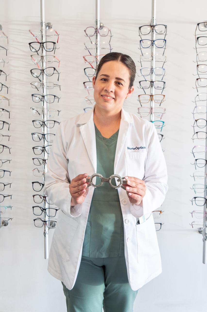 Lic. Opt. Erika Martínez, optometrista de Norte Ópticos, con un armazón de pruebas frente a la exhibición de armazones